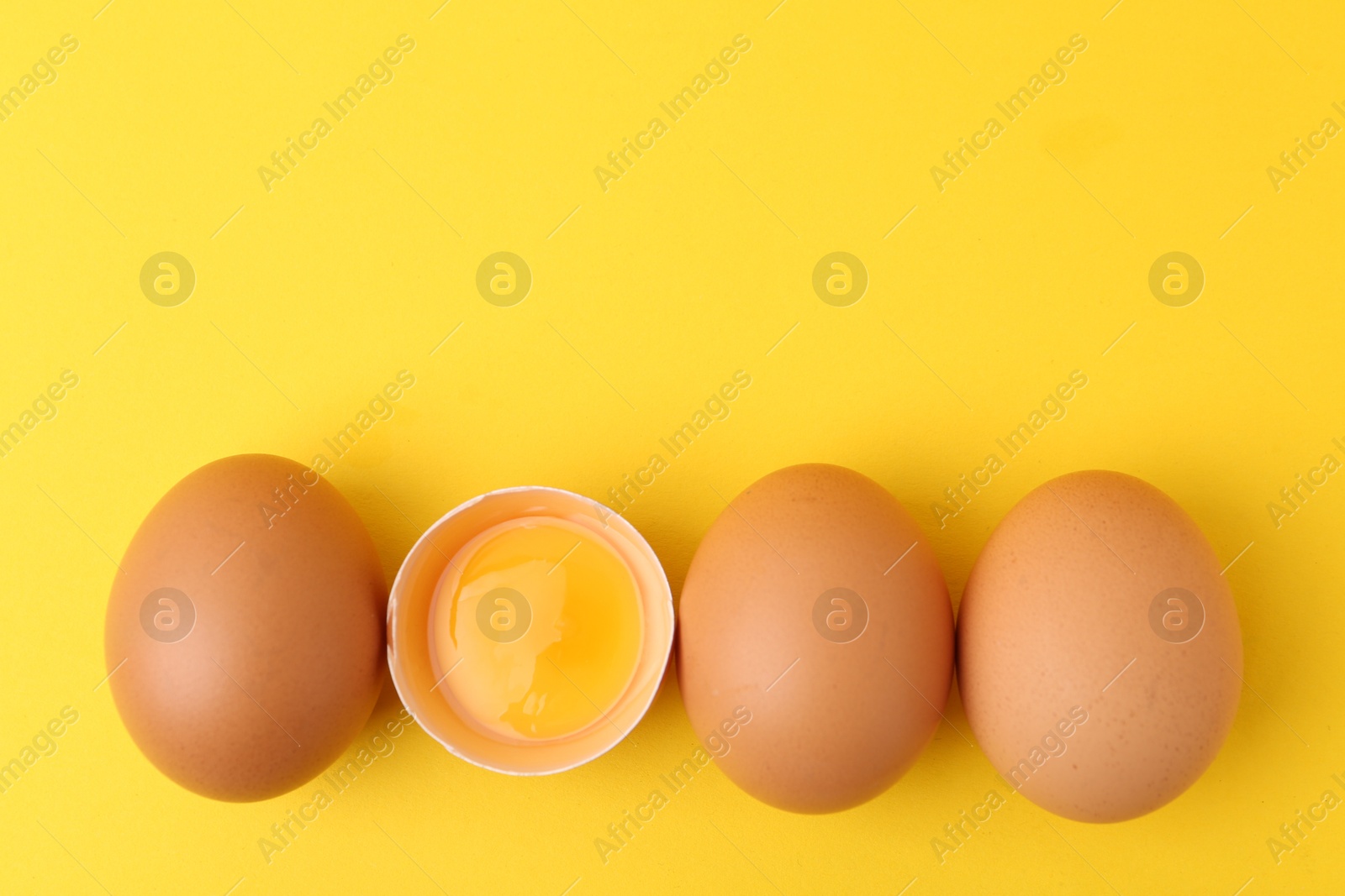 Whole and broken chicken eggs on yellow background, top view. Space for text Photo of Whole and broken chicken eggs on yellow background, top view. Space for text