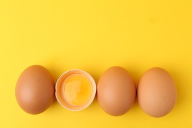 Photo of Whole and broken chicken eggs on yellow background, top view. Space for text