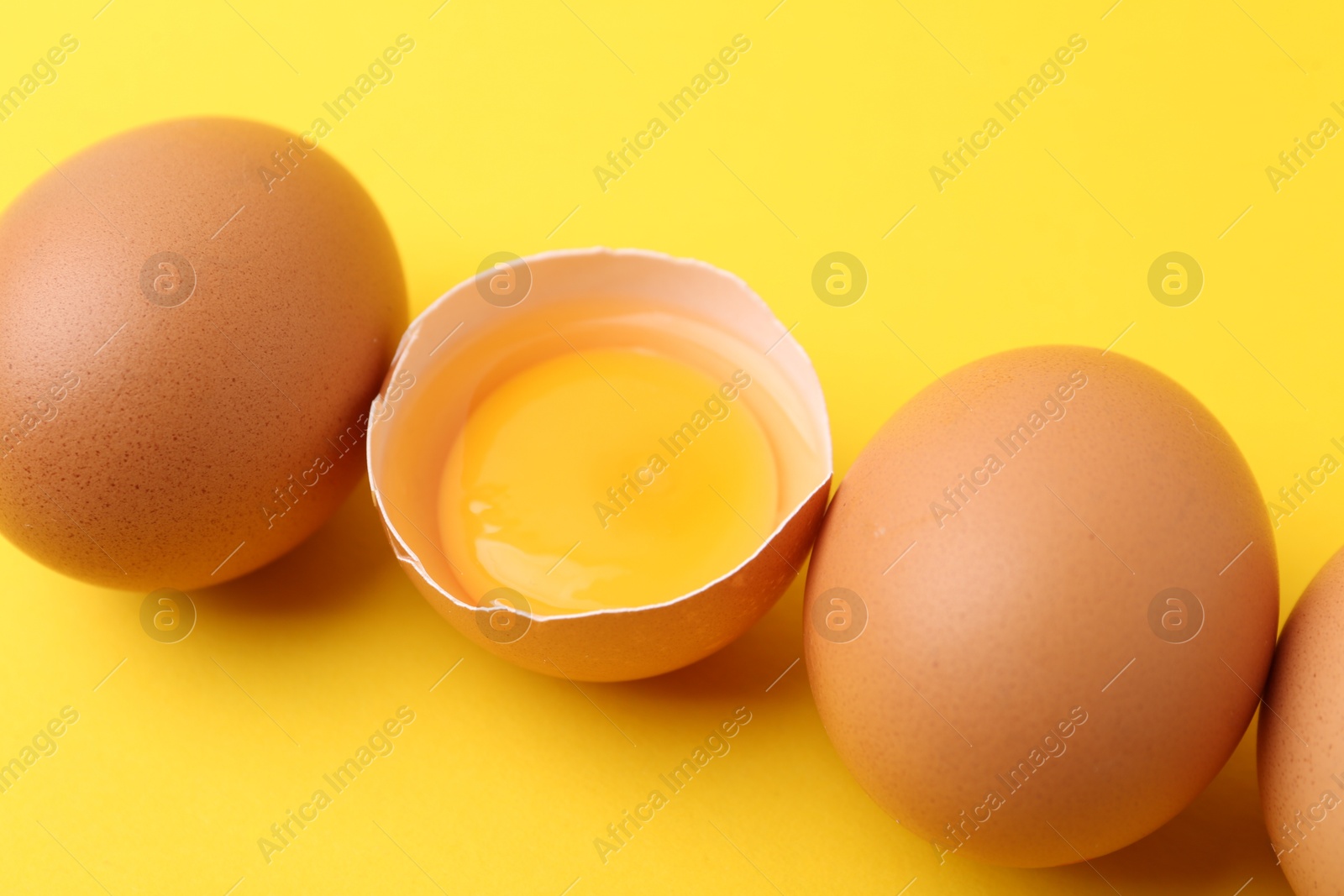Whole and broken chicken eggs on yellow background, closeup Photo of Whole and broken chicken eggs on yellow background, closeup