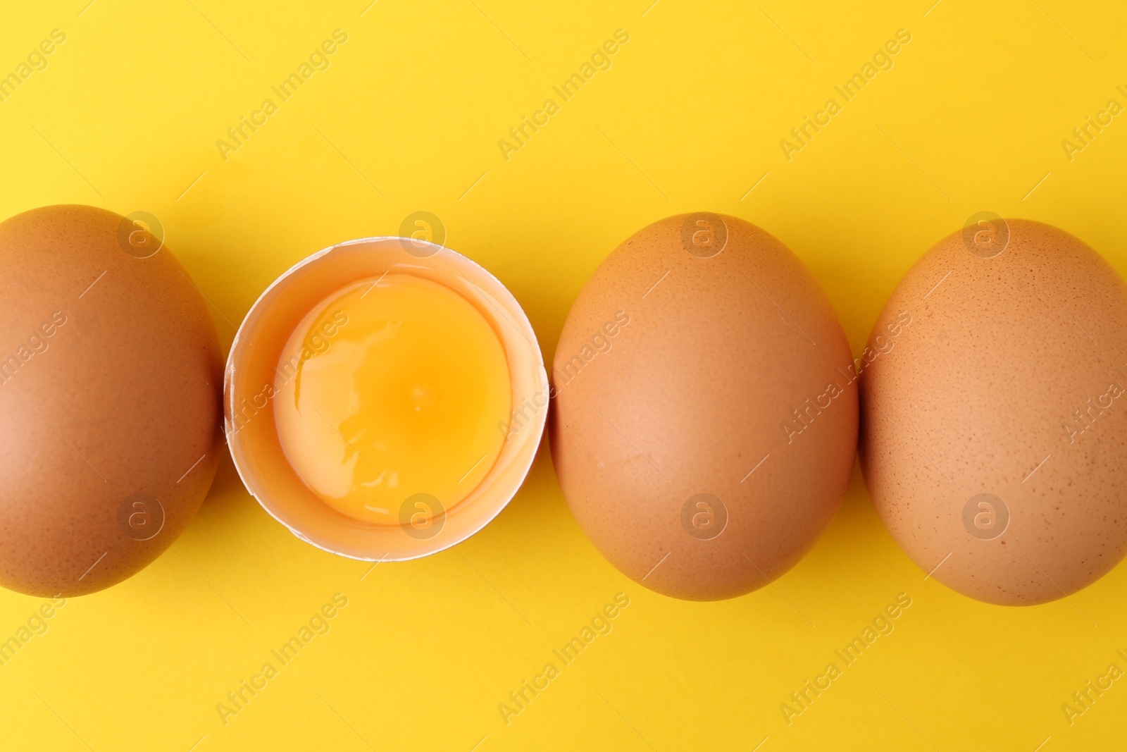 Whole and broken chicken eggs on yellow background, top view Photo of Whole and broken chicken eggs on yellow background, top view