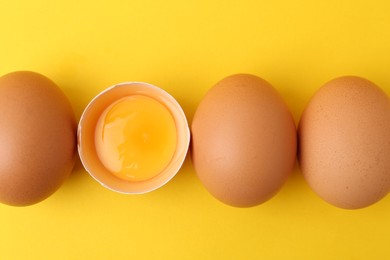 Photo of Whole and broken chicken eggs on yellow background, top view