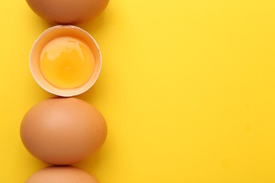 Photo of Whole and broken chicken eggs on yellow background, top view. Space for text