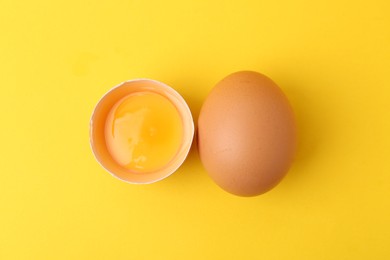 Photo of Whole and broken chicken eggs on yellow background, top view