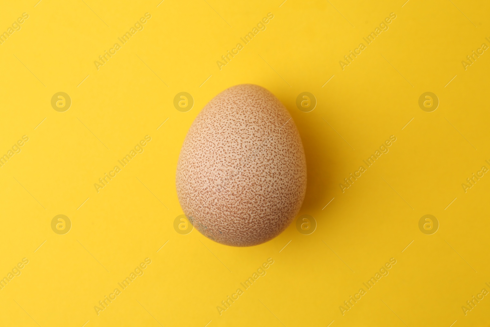 One raw chicken egg on yellow background, top view Photo of One raw chicken egg on yellow background, top view