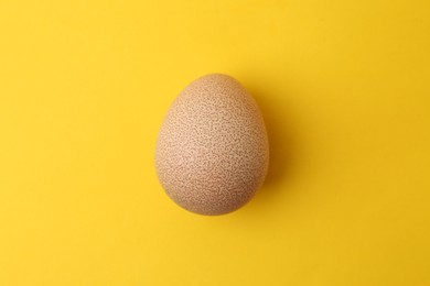 Photo of One raw chicken egg on yellow background, top view