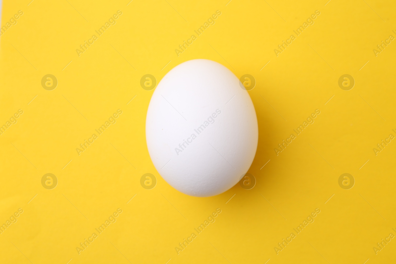 One raw chicken egg on yellow background, top view Photo of One raw chicken egg on yellow background, top view