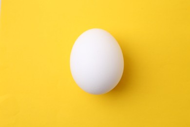 Photo of One raw chicken egg on yellow background, top view
