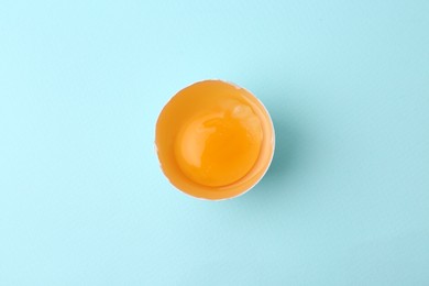 Photo of One broken chicken egg on light blue background, top view