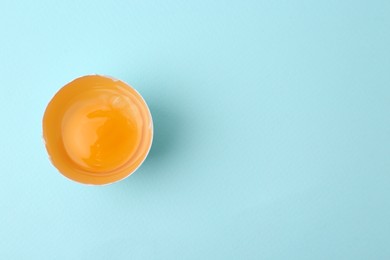 Photo of One broken chicken egg on light blue background, top view. Space for text