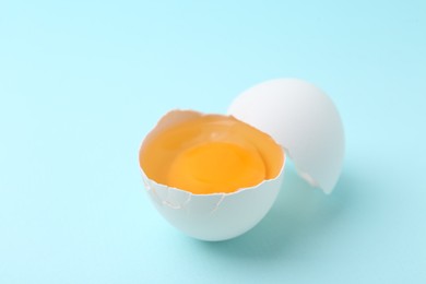 Photo of One broken chicken egg on light blue background, closeup