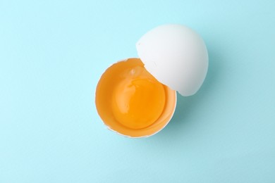 Photo of One broken chicken egg on light blue background, top view