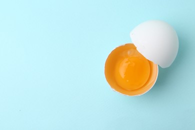 Photo of One broken chicken egg on light blue background, top view. Space for text