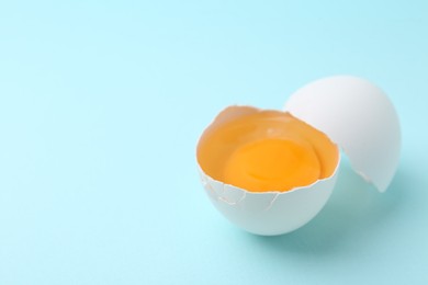 Photo of One broken chicken egg on light blue background, closeup. Space for text