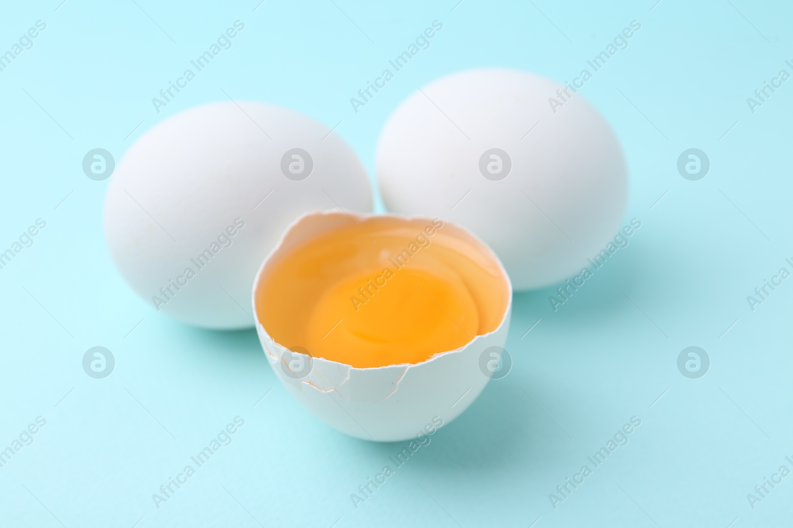 Photo of Whole and broken chicken eggs on light blue background, closeup
