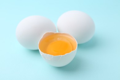 Photo of Whole and broken chicken eggs on light blue background, closeup