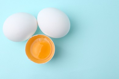 Photo of Whole and broken chicken eggs on light blue background, top view. Space for text