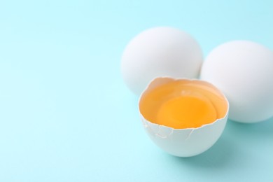 Photo of Whole and broken chicken eggs on light blue background, closeup. Space for text
