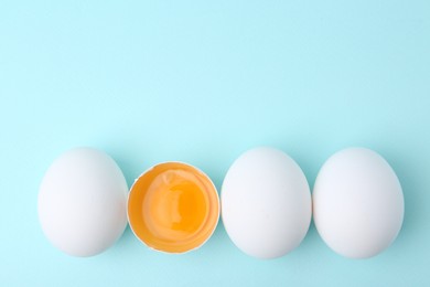 Photo of Whole and broken chicken eggs on light blue background, top view. Space for text