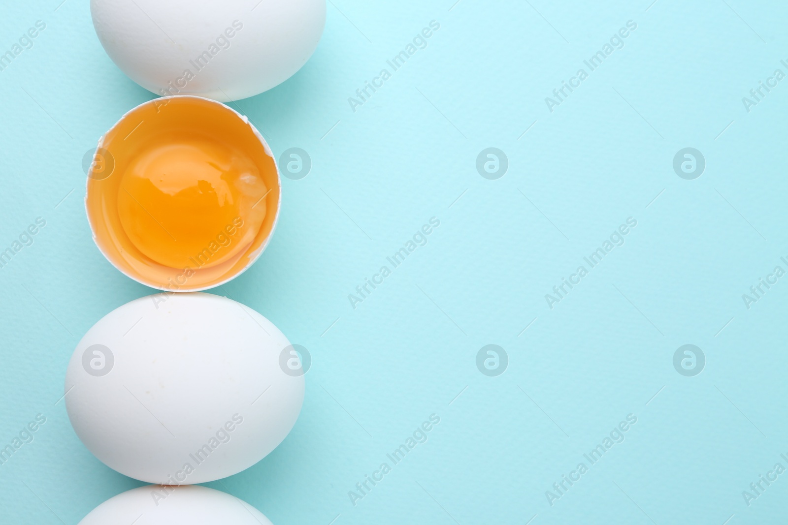 Photo of Whole and broken chicken eggs on light blue background, top view. Space for text