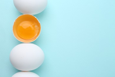 Photo of Whole and broken chicken eggs on light blue background, top view. Space for text