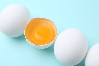 Photo of Whole and broken chicken eggs on light blue background, closeup