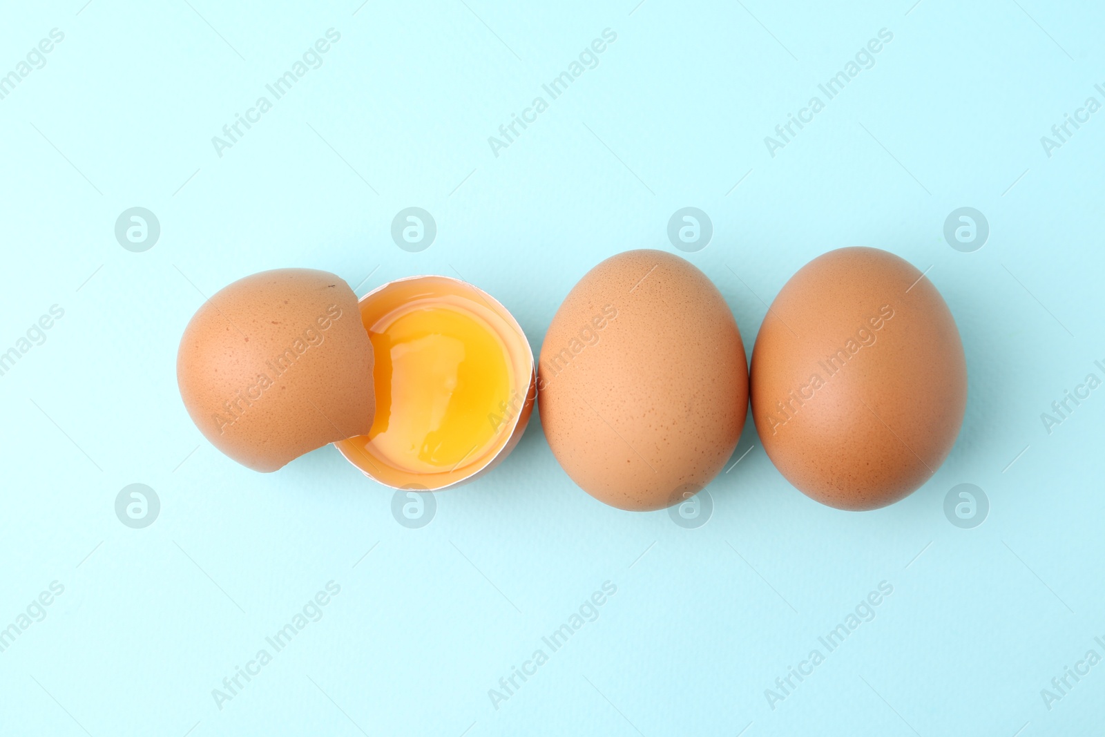 Whole and broken chicken eggs on light blue background, top view Photo of Whole and broken chicken eggs on light blue background, top view
