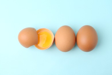 Photo of Whole and broken chicken eggs on light blue background, top view