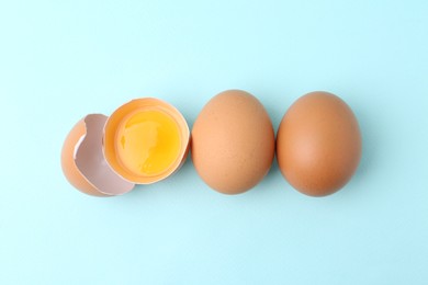 Photo of Whole and broken chicken eggs on light blue background, top view
