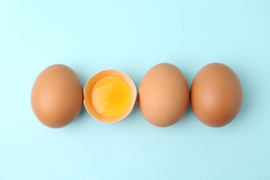Photo of Whole and broken chicken eggs on light blue background, top view