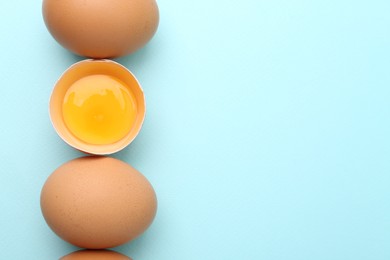 Photo of Whole and broken chicken eggs on light blue background, top view. Space for text