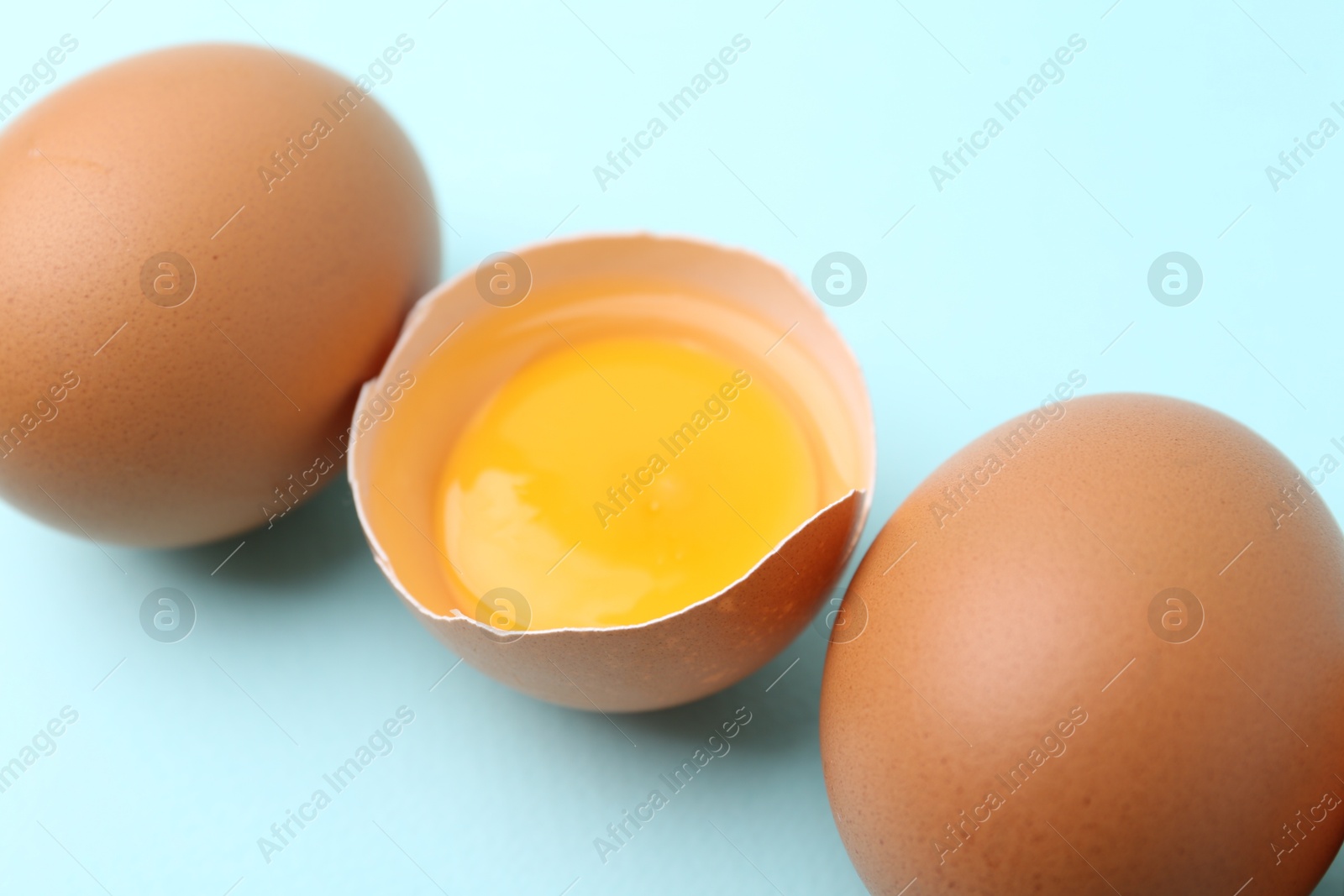 Photo of Whole and broken chicken eggs on light blue background, closeup