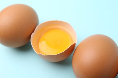 Photo of Whole and broken chicken eggs on light blue background, closeup