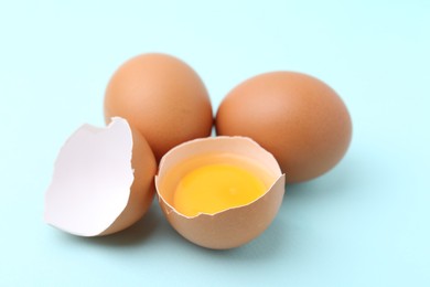 Photo of Whole and broken chicken eggs on light blue background, closeup