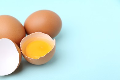 Photo of Whole and broken chicken eggs on light blue background, closeup. Space for text