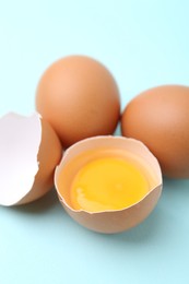 Photo of Whole and broken chicken eggs on light blue background, closeup