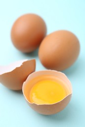 Photo of Whole and broken chicken eggs on light blue background, closeup