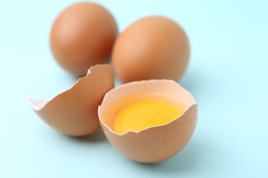 Photo of Whole and broken chicken eggs on light blue background, closeup