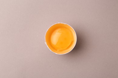 Photo of One broken chicken egg on grey background, top view