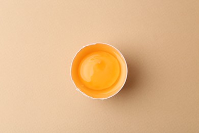 Photo of One broken chicken egg on beige background, top view