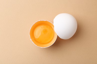 Photo of One broken chicken egg on beige background, top view
