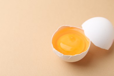 Photo of Broken chicken egg on beige background, closeup. Space for text