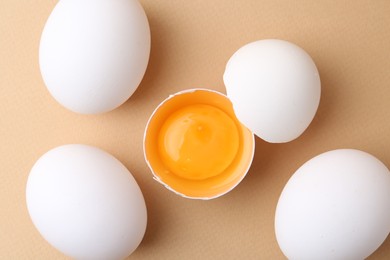 Photo of Whole and broken chicken eggs on beige background, top view