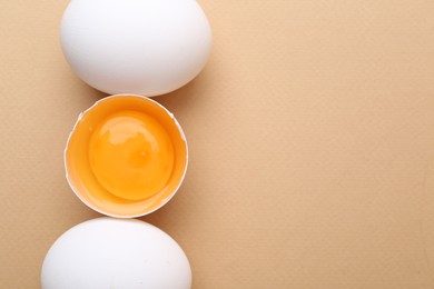Photo of Whole and broken chicken eggs on beige background, top view. Space for text
