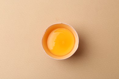 Photo of One broken chicken egg on beige background, top view