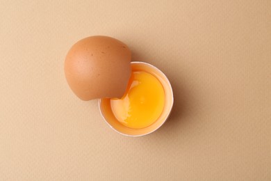 Photo of One broken chicken egg on beige background, top view