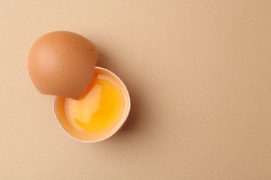 Photo of One broken chicken egg on beige background, top view. Space for text