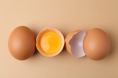 Photo of Whole and broken chicken eggs on beige background, top view