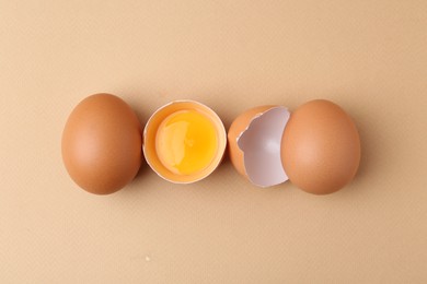 Photo of Whole and broken chicken eggs on beige background, top view