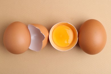 Photo of Whole and broken chicken eggs on beige background, top view