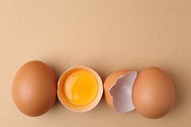 Photo of Whole and broken chicken eggs on beige background, top view. Space for text